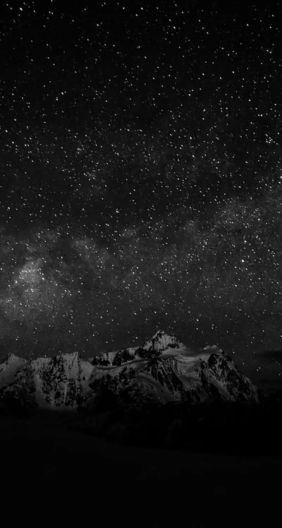 Thousands of stars crowd a monochrome night sky, the jagged peaks below reduced to a low grey band across the bottom third.