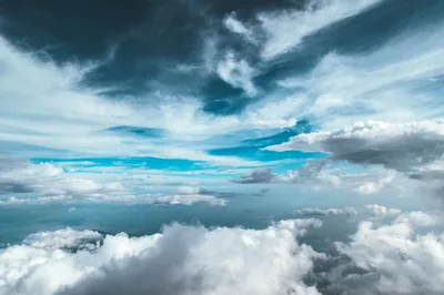Shot between two cloud decks: bright cumulus below, streaked grey above, and a band of clear turquoise opening across the middle.