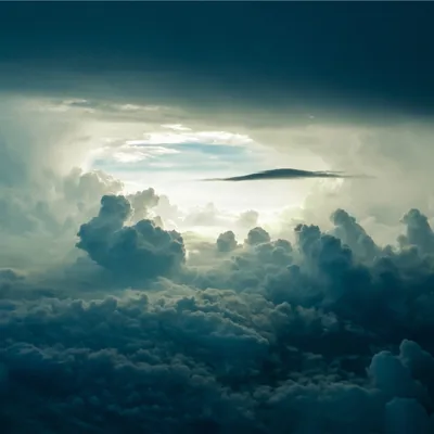 Shot from between two cloud layers: sunlit cumulus below, a dark ceiling above, and one lens-shaped cloud floating alone in the bright gap at centre.