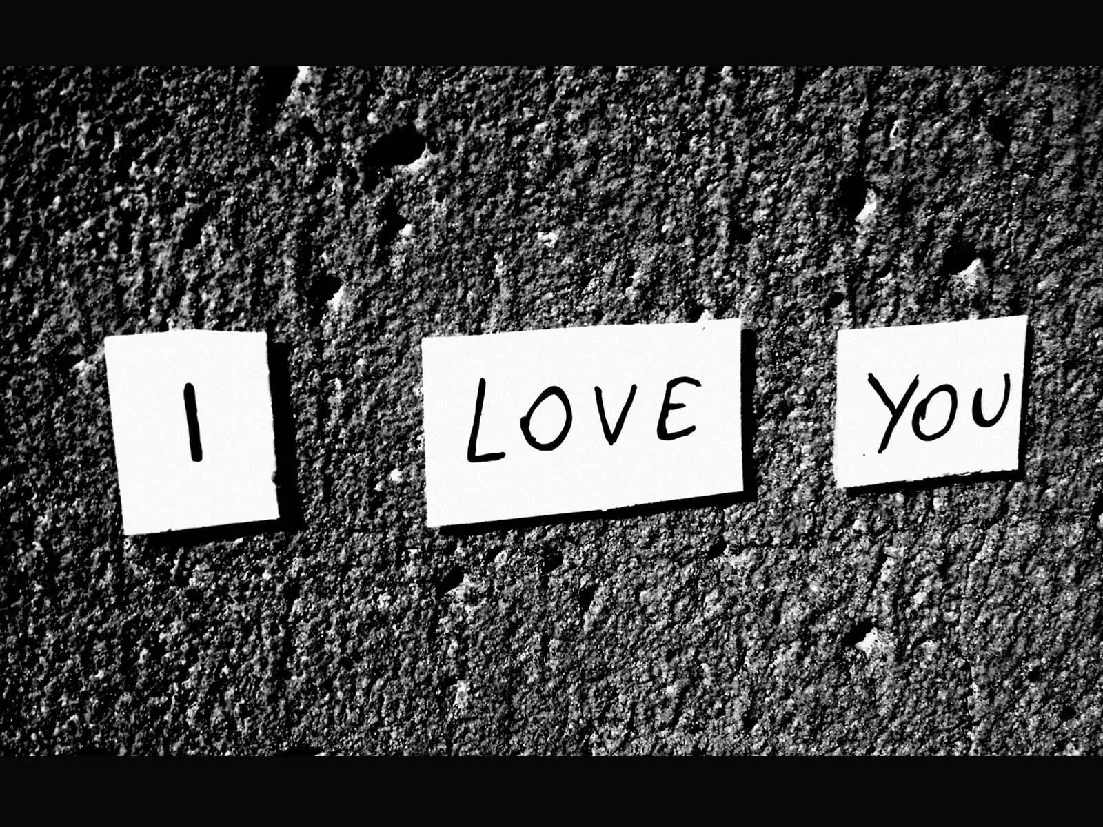 Three paper cards taped to rough concrete spell out the words, shot in high-contrast monochrome with the corners falling into shadow.