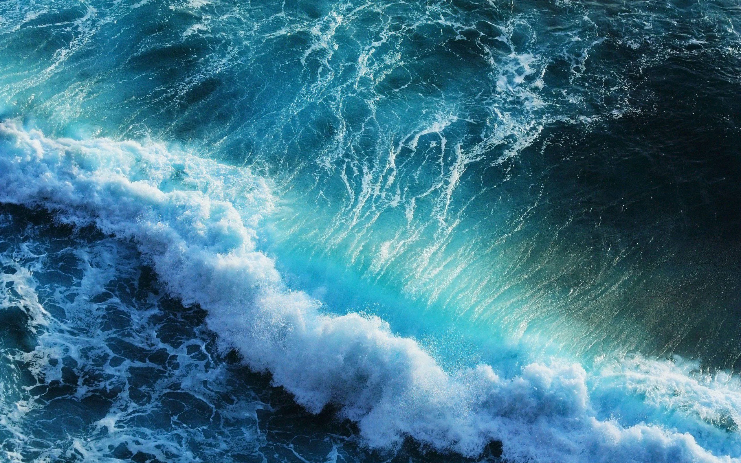 A collapsing crest drags streaks of whitewater across dark teal sea, the foam cutting a rough diagonal through the frame.