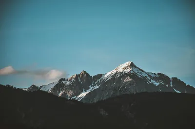 A snow-dusted peak catches fading light against a teal sky, the solid black forest silhouette along the bottom suiting OLED screens.