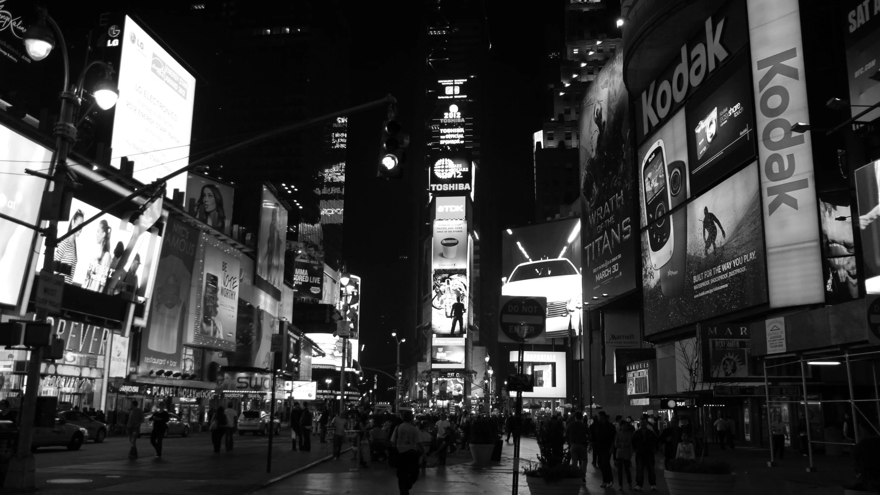 Advertising screens stack up both sides of a packed street, their glare washing the pavement while the sky between the towers stays black.