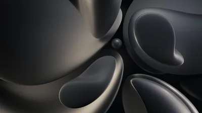 Rounded graphite forms press against each other with soft hollows scooped out of them, a small sphere resting in the gap at the centre.