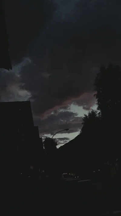 The last purple light breaks through heavy cloud over a street, rooftops and trees already fallen into silhouette.