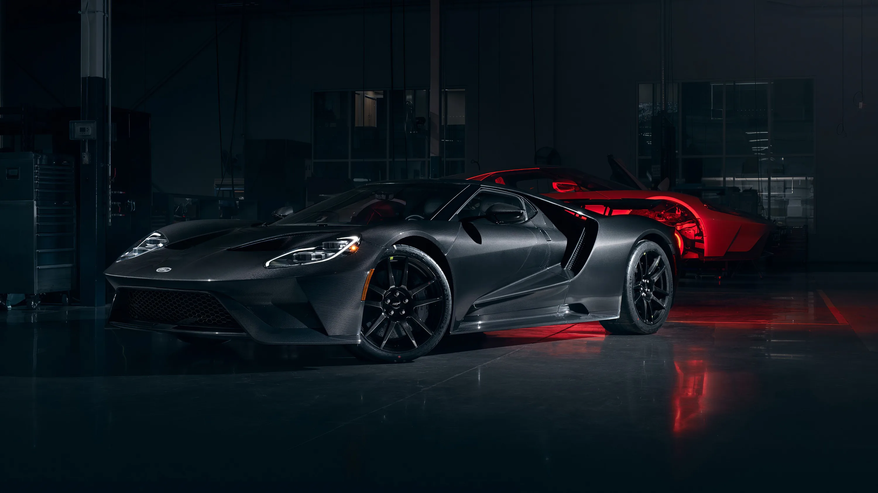 A black Ford GT sits in shadow with red striping along its flying buttresses, a second red car dissolving into the dark behind it.
