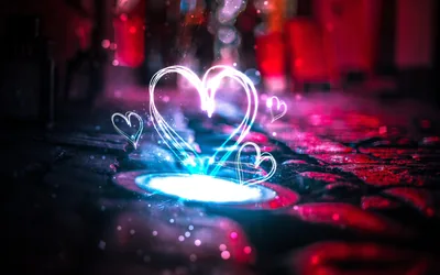 Hearts traced in white light float above a glowing drain on wet cobblestones, pink and blue neon smeared out of focus behind them.