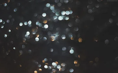 Out-of-focus white and amber orbs drift across a dark field, dim enough that home-screen text stays legible over any part of it.