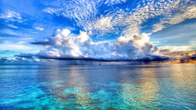Rows of small clouds lead back to one dense storm cell dumping rain at the horizon, the still lagoon mirroring it all in teal and gold.
