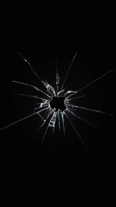 A punched hole sits just above centre with cracks radiating out across black glass, shards catching thin white light along their broken edges.