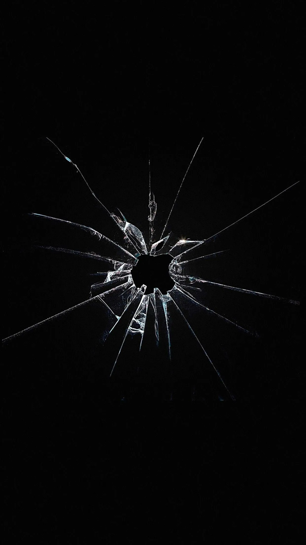 A punched hole sits just above centre with cracks radiating out across black glass, shards catching thin white light along their broken edges.