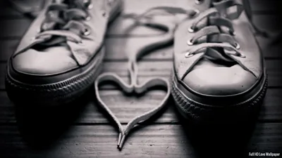 Two canvas sneakers on wooden planks with their laces looped into a heart between them, shot in soft monochrome.