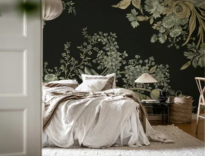 Sage and cream botanicals climb a near-black mural behind an unmade white bed, the largest blooms gathered in the top right corner.
