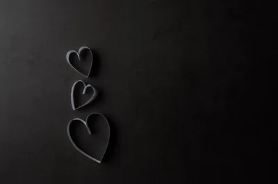 Three cut-paper hearts run down the left side of a dark slate surface, the whole right half left empty for desktop icons.