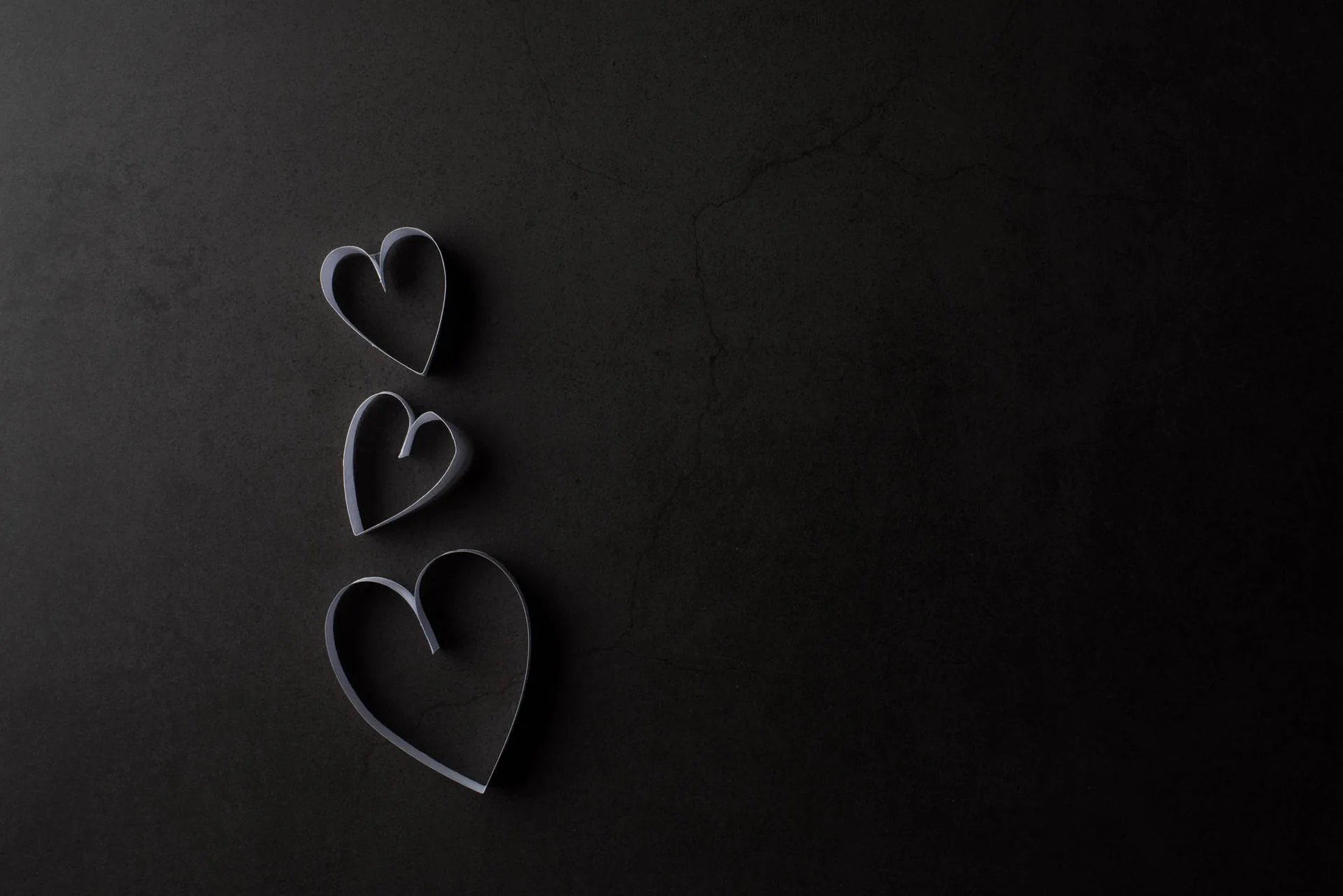 Three cut-paper hearts run down the left side of a dark slate surface, the whole right half left empty for desktop icons.