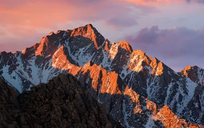 Low sun rakes across a fractured granite face under dusty pink clouds, in the style of the macOS Sierra desktop background.