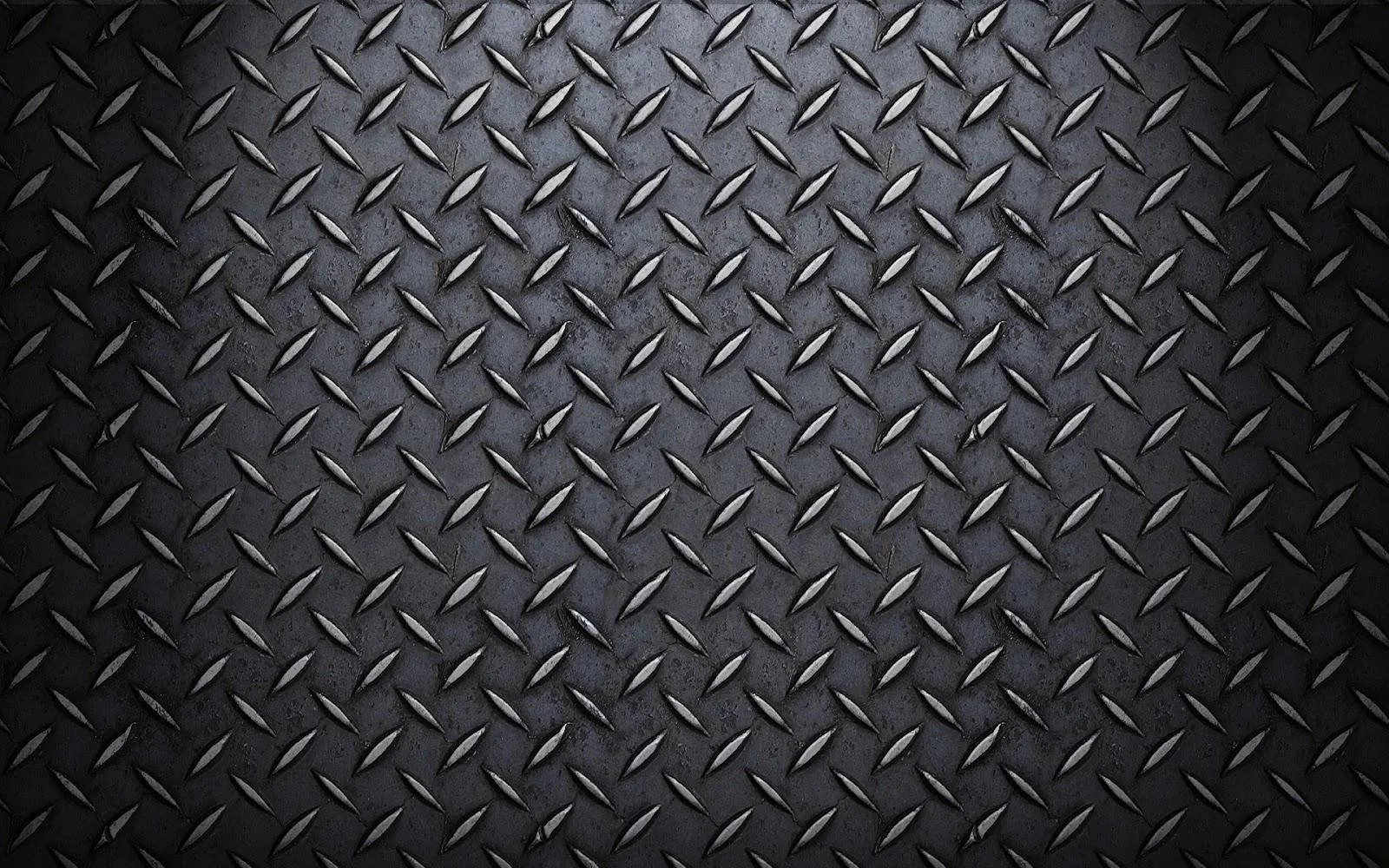 Raised diamond treads cover a dark steel plate, worn brighter through the centre and dimming to black at every corner.
