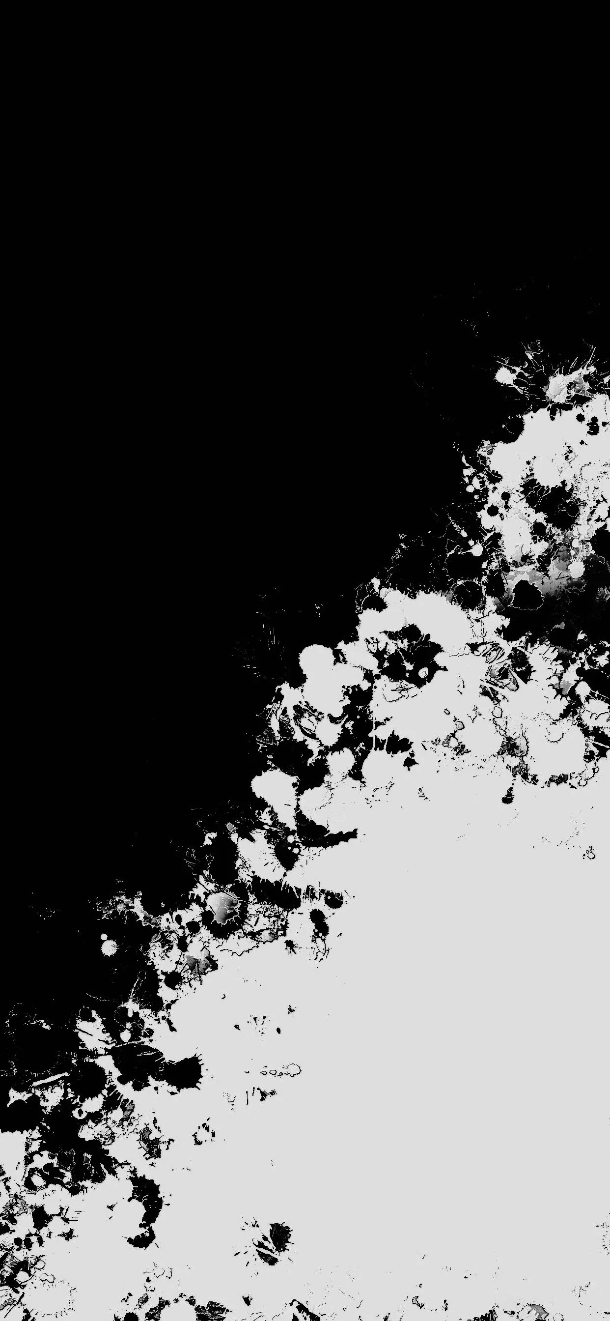 A diagonal split runs corner to corner, black above and white below, the boundary broken into scattered ink blots and specks.