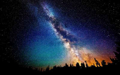 The galactic core burns orange behind silhouetted conifers while the sky shifts from teal to deep blue toward the upper left corner.