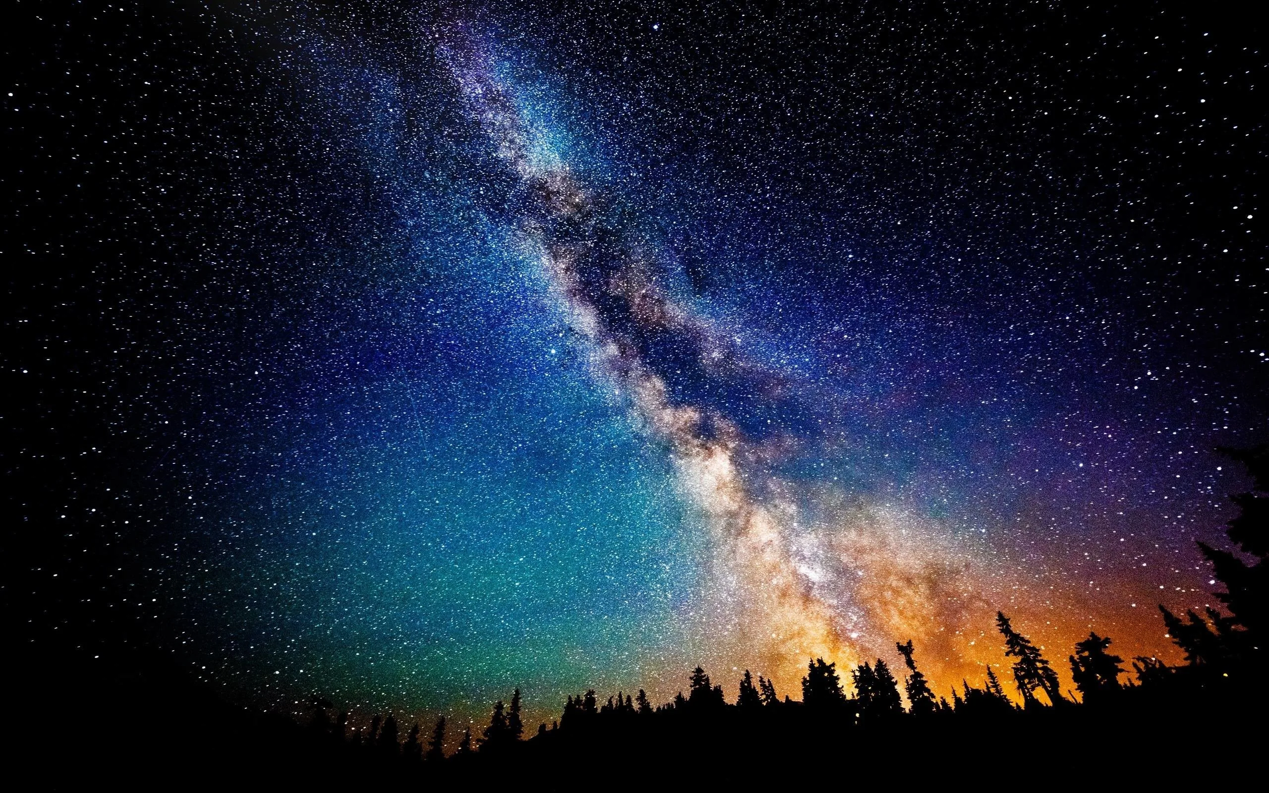 The galactic core burns orange behind silhouetted conifers while the sky shifts from teal to deep blue toward the upper left corner.