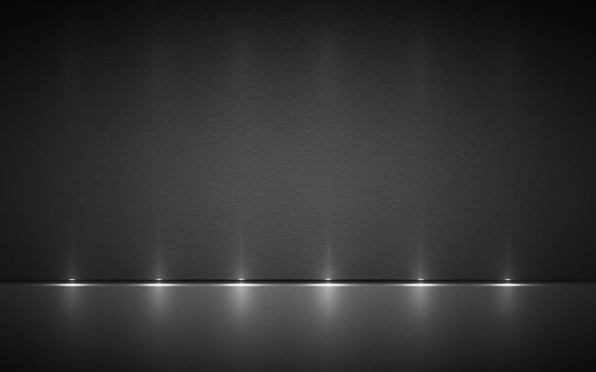 Six small downlights spaced along the base of a dark grey wall, each reflected in the glossy floor, while the upper two-thirds stays dim for desktop icons.