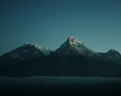 A moonlit snow ridge line runs across the middle under a deep blue-green night sky, mist pooling below and the sky clear enough for a clock.