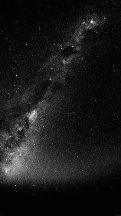 The galactic band cuts diagonally across a black-and-white sky, its dust lanes clearly split, with a soft ground glow along the bottom edge.