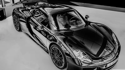 High angle on a Porsche hybrid roadster in a showroom, roof panels and windscreen throwing back the overhead lights as the polished floor drops away pure white.
