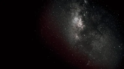 The Milky Way core burns in the upper right while the rest of the sky stays close to black, a faint red airglow bleeding in from the left.
