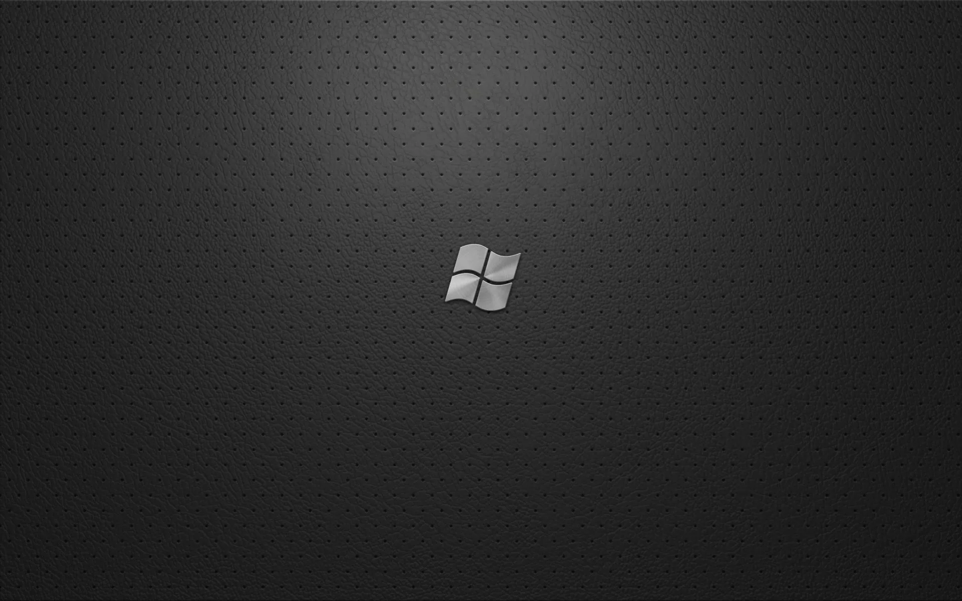A small pale four-flag Windows logo sits at the centre of a charcoal cloth weave, the texture lightening slightly behind it.