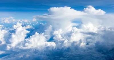 A wall of towering cumulus seen from cruising altitude, sunlit white tops rolling toward a patch of blue in the upper left.