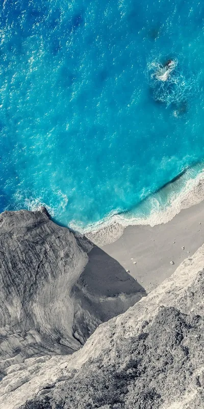 Vivid blue water meets a scree slope and grey cliff face from above, the diagonal split giving the frame its structure.