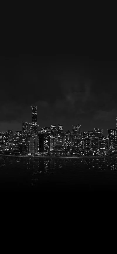 A row of lit towers sits low in the tall frame, its reflection breaking up in the water while the sky above stays near black.