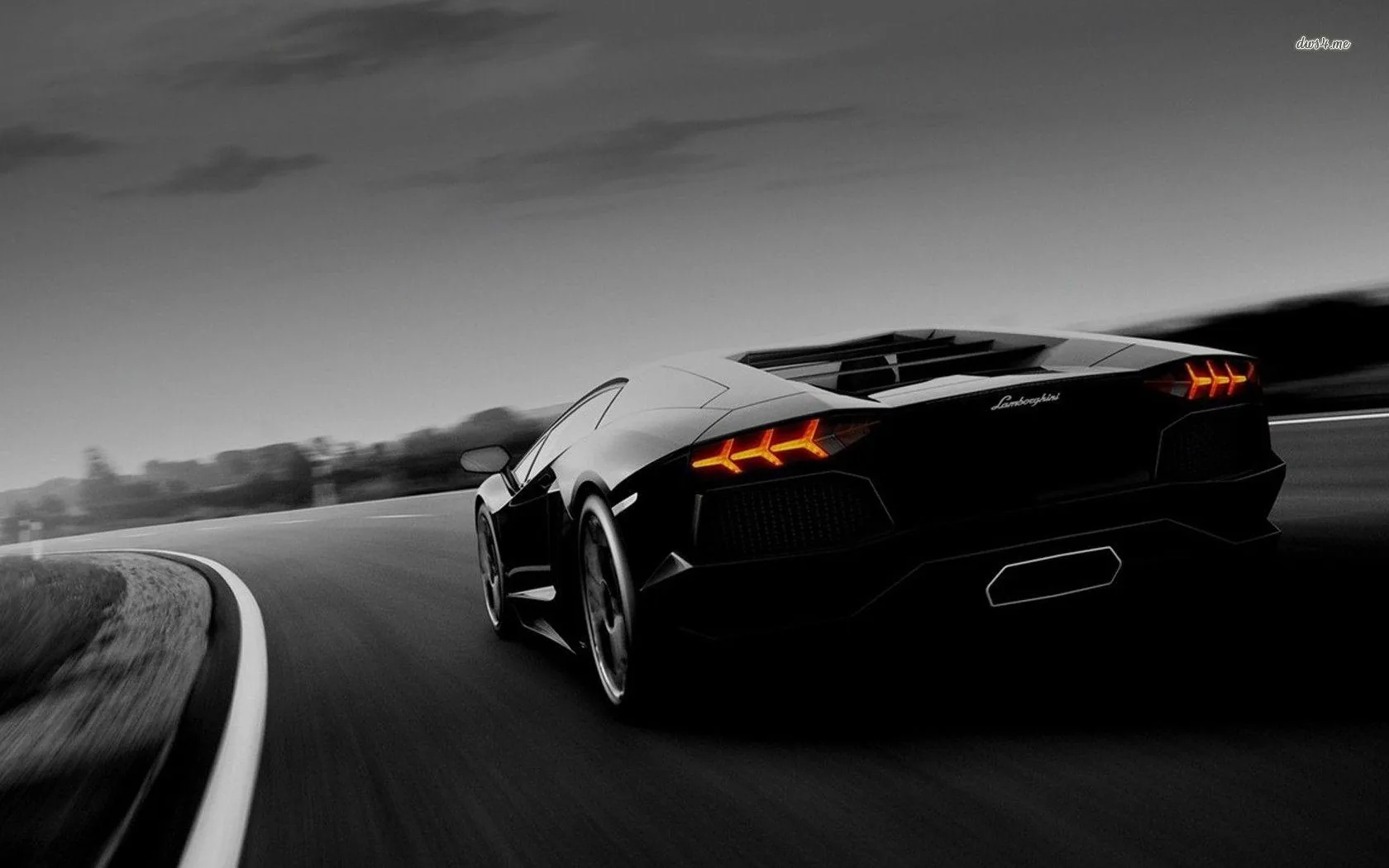 Shot from behind on a sweeping road, the Aventador's hexagonal tail lights and quad exhaust glow orange while the sky and verge blur to grey.