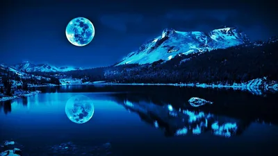 A full moon hangs above snow-covered peaks and mirrors in the still lake below, the whole scene washed in cold blue night light.