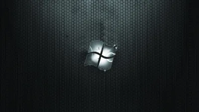 A brushed metal Windows emblem hangs at the centre of a dark honeycomb mesh panel, light falling off sharply toward the corners.
