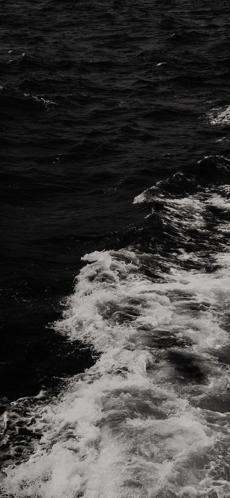 White foam trails diagonally across near-black sea, shot from above so the wake fills the lower half.