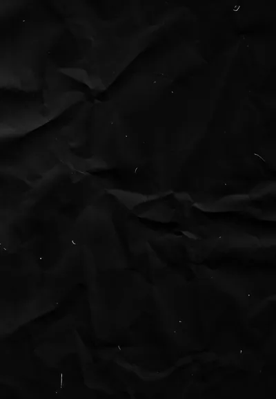 Black paper creased and folded across the frame, the ridges catching just enough light to show the crumple lines and a few flecks of white dust.