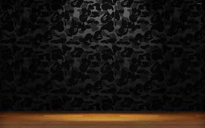 A wall papered in black camouflage print stands behind a warm wooden floor, the only colour in an otherwise dark room.