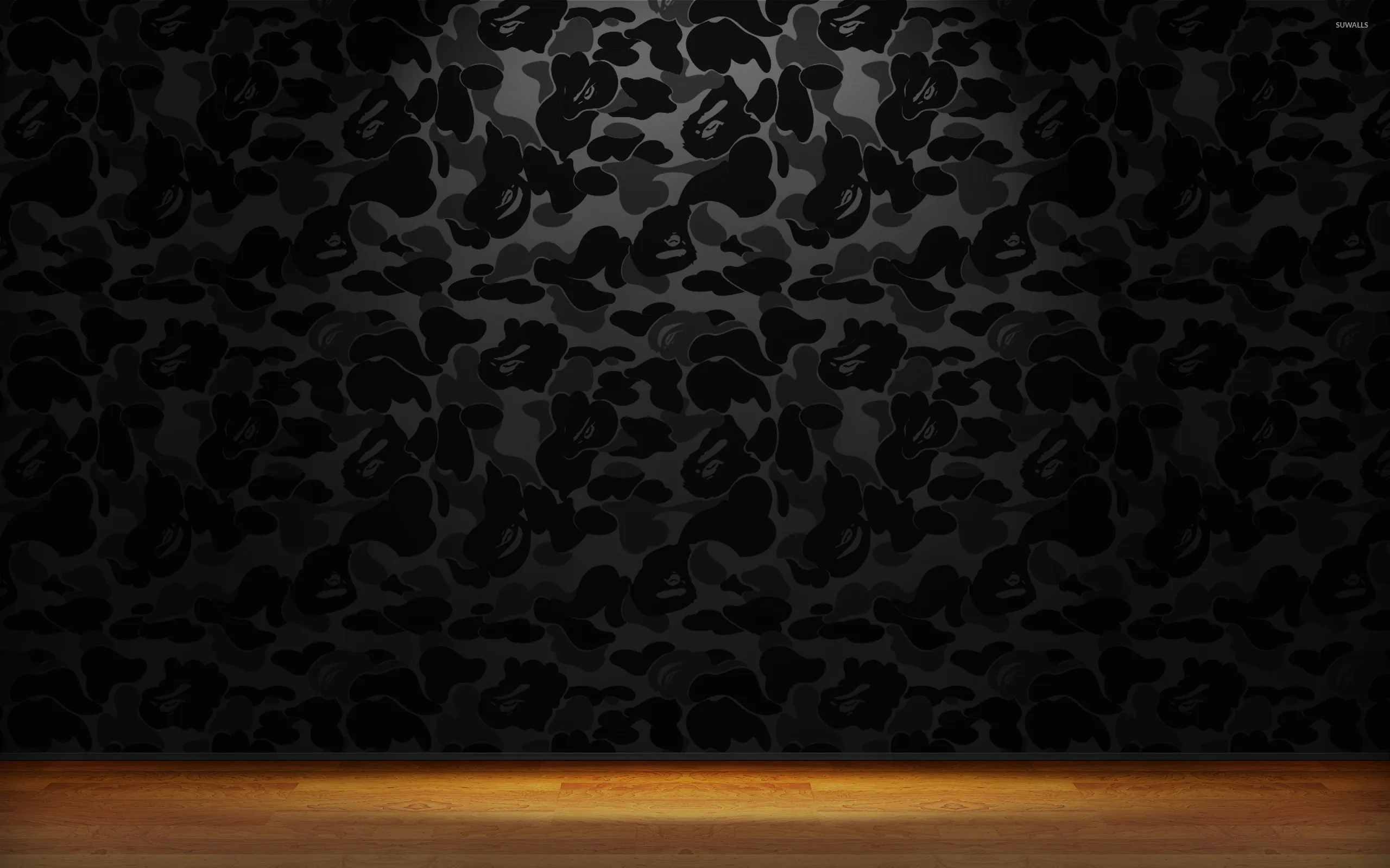 A wall papered in black camouflage print stands behind a warm wooden floor, the only colour in an otherwise dark room.