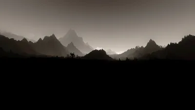 Jagged peaks fade back through brown haze in three tones, with a pitch-dark foreground ridge running along the bottom of the frame.