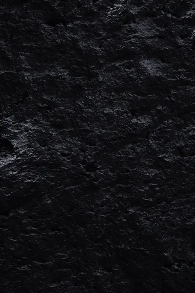 Cracked volcanic rock fills a tall frame, wet-looking patches on the left catching light while the rest stays matte and unlit.