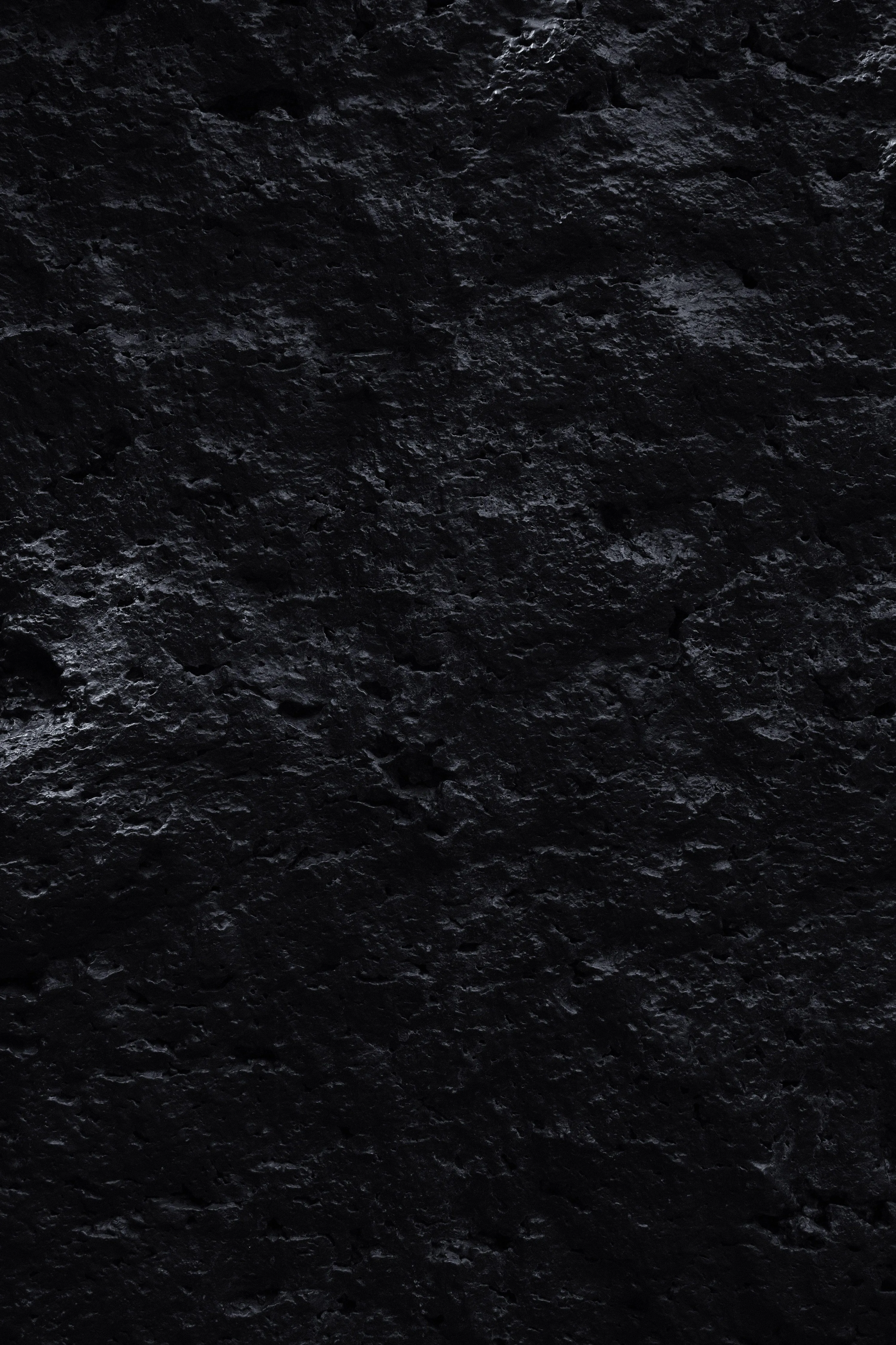 Cracked volcanic rock fills a tall frame, wet-looking patches on the left catching light while the rest stays matte and unlit.