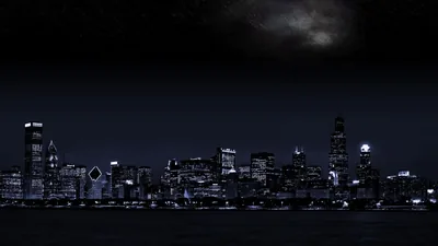 Chicago's skyline glows in cold blue against a black sky, moonlit cloud showing only along the top edge above the towers.
