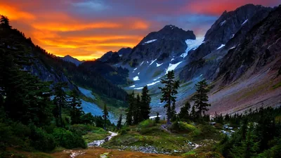 Orange and red clouds burn above snow-patched peaks while a stream threads the green basin below, the dark valley floor hiding desktop clutter.