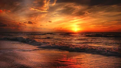 Ragged clouds smoulder in red and gold above lines of breaking waves, the light pooling in reflections on the dark wet beach.