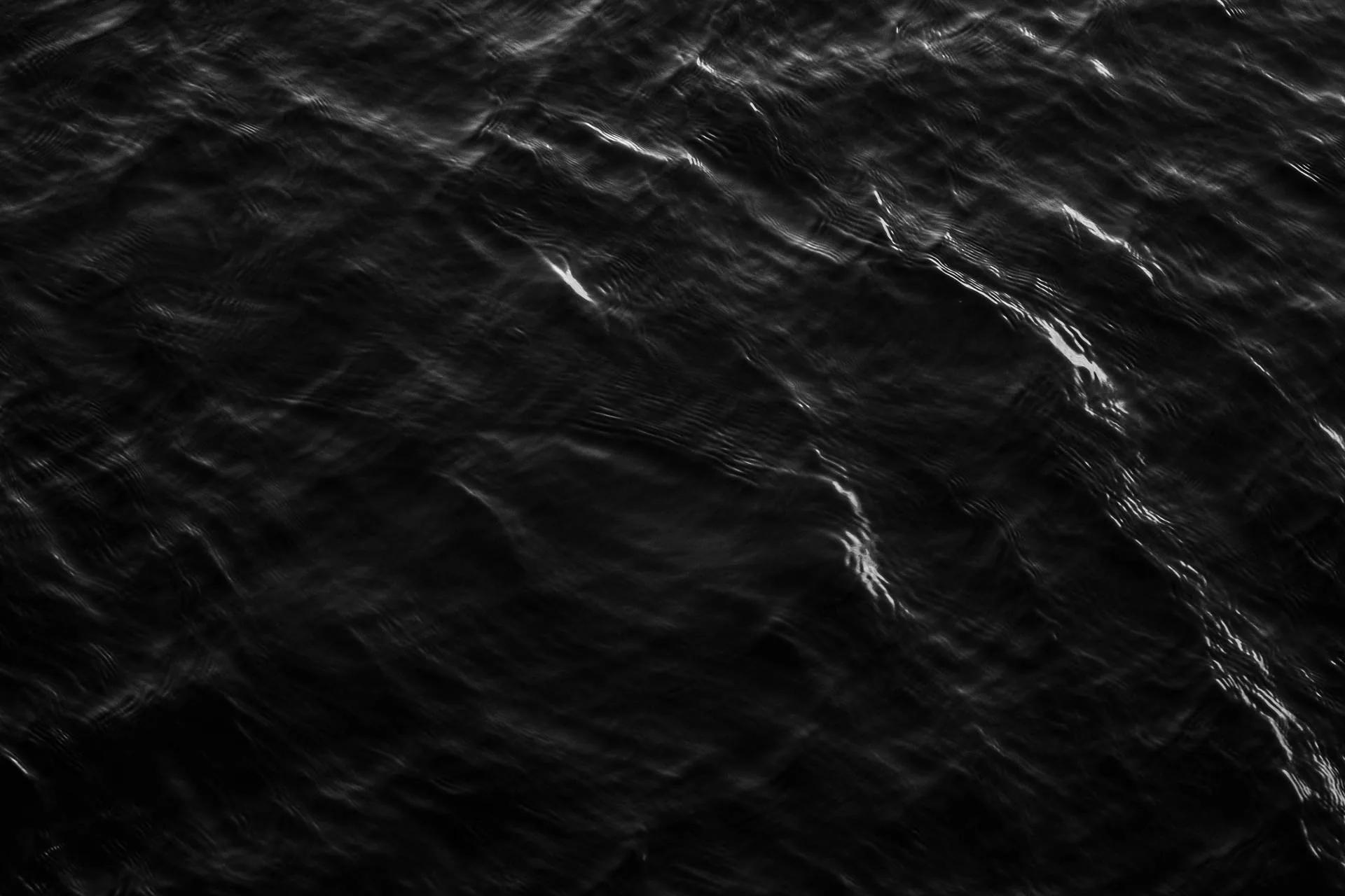 Faint white crests catch the light across near-black water, the ripples running diagonally while the lower corners stay unlit.