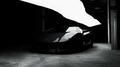 High-contrast monochrome: a wedge-shaped Lamborghini parked under a concrete ramp, the bright floor slab behind it turning the whole car into a black shape.
