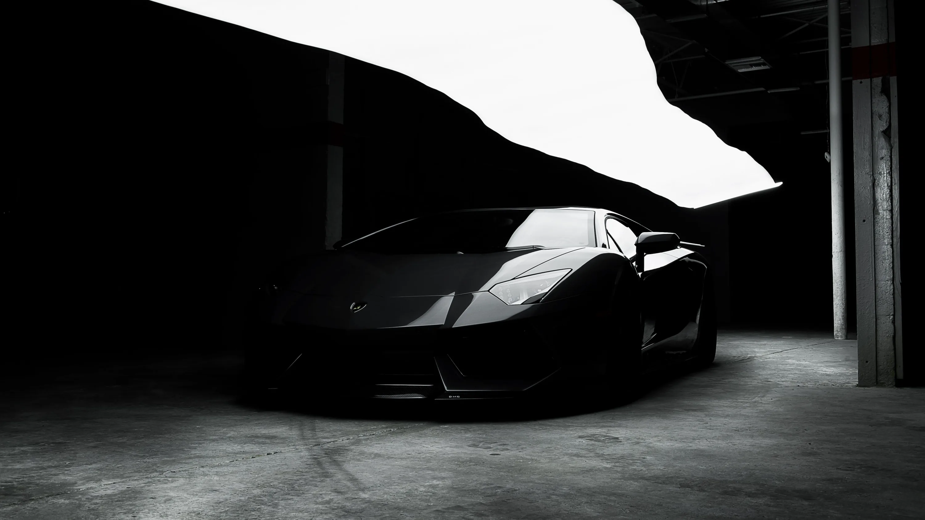 High-contrast monochrome: a wedge-shaped Lamborghini parked under a concrete ramp, the bright floor slab behind it turning the whole car into a black shape.