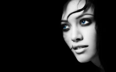 A woman's face leans in from the right of a black frame, her blue eyes the only colour; the entire left half is solid black.